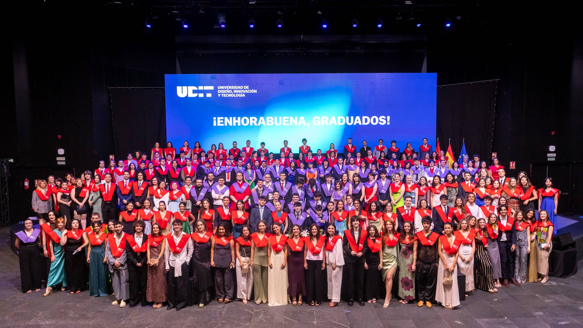 Una ceremonia de graduación con un grupo numeroso de graduados en un escenario.