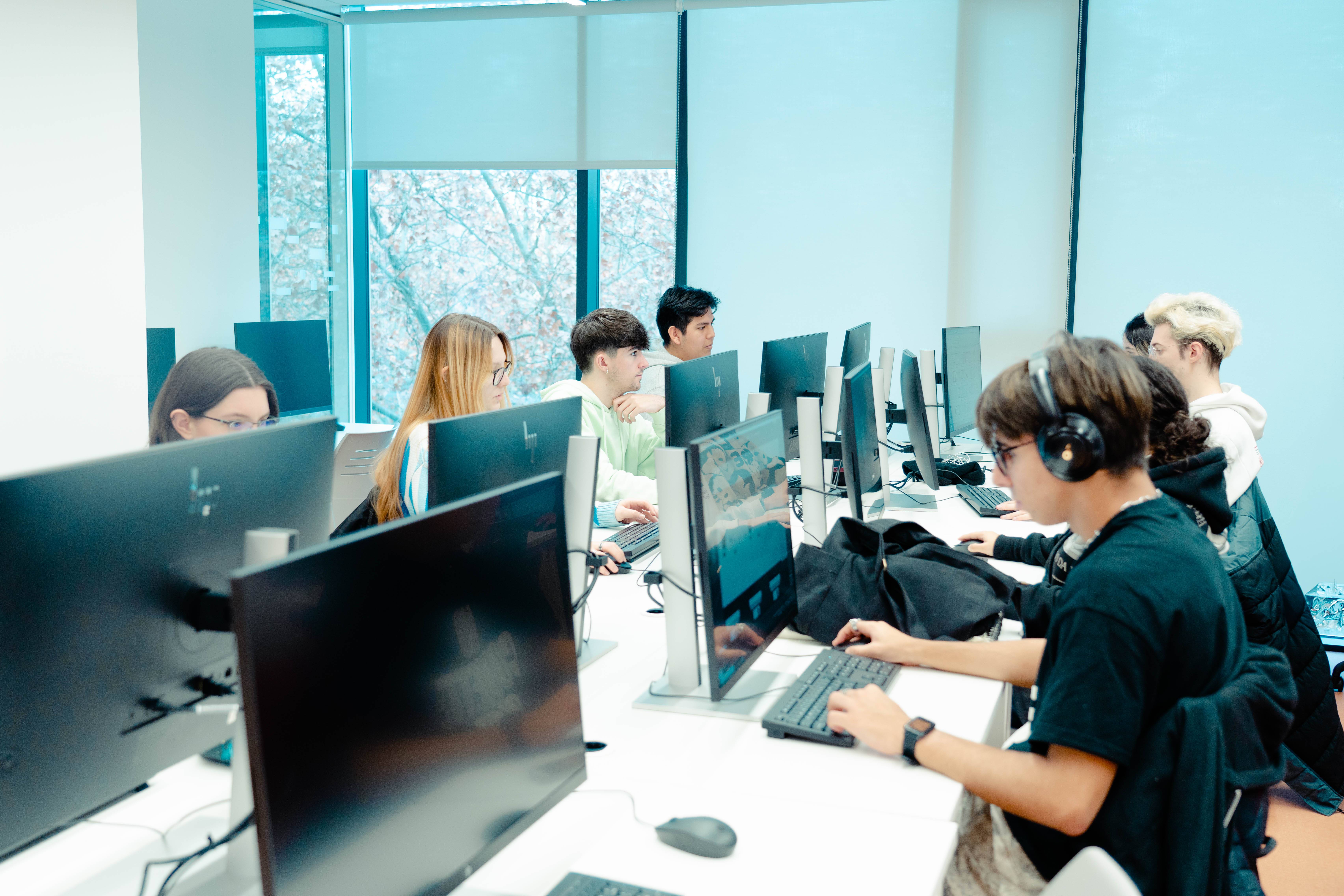 Grupo de estudiantes trabajando en computadoras en un aula moderna.