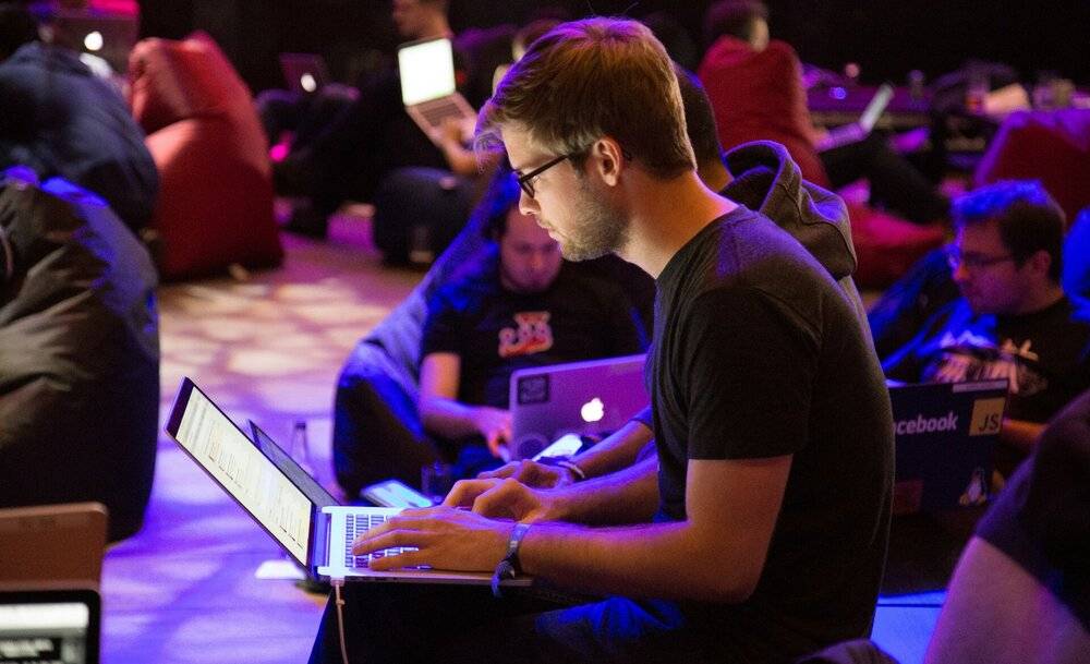Un grupo de personas trabaja en computadoras portátiles en un ambiente relajado con luces de fondo.