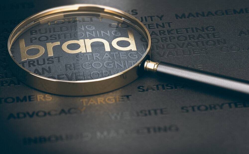 Una lupa enfoca la palabra 'brand' sobre un fondo lleno de términos de marketing.