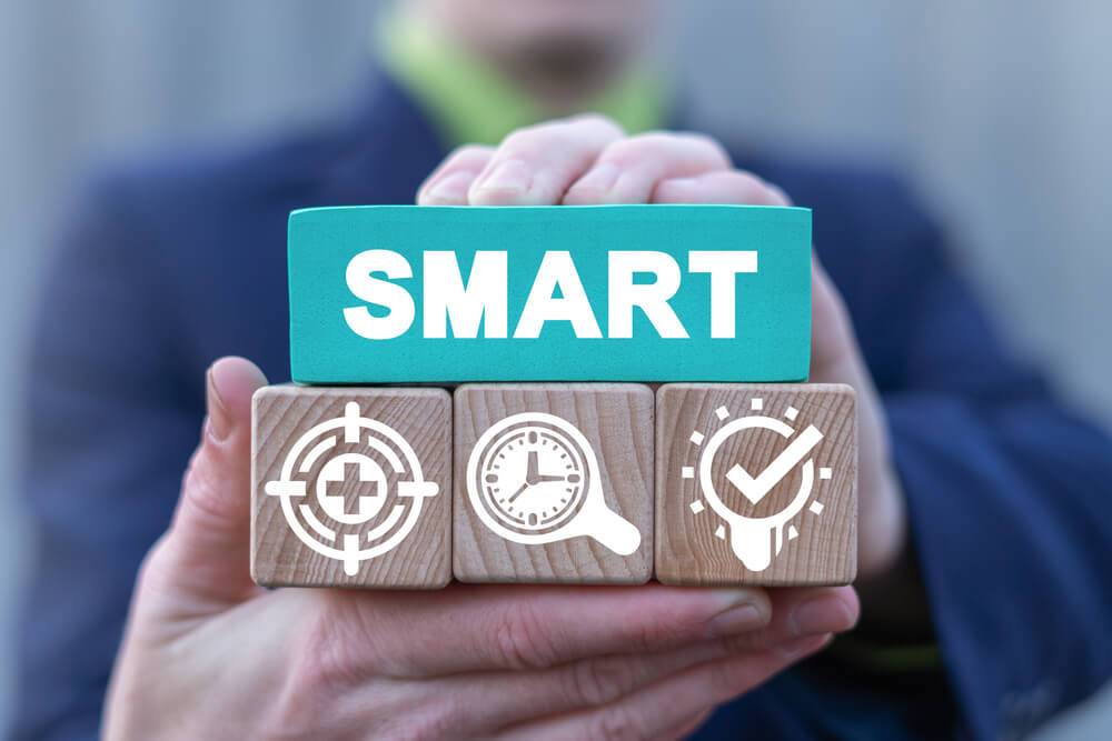 Una persona sostiene bloques de madera con la palabra SMART y símbolos que representan objetivos claros y medibles.