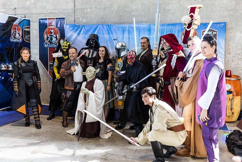 Un grupo de personas vestidas con trajes de personajes icónicos de la saga Star Wars posan con sables de luz en un evento de cosplay.