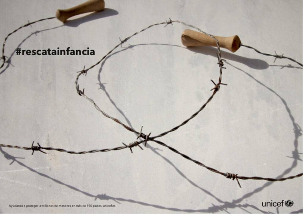 Imagen que muestra alambre de espino formando un patrón en la superficie, con un lema de UNICEF sobre la protección de la infancia.