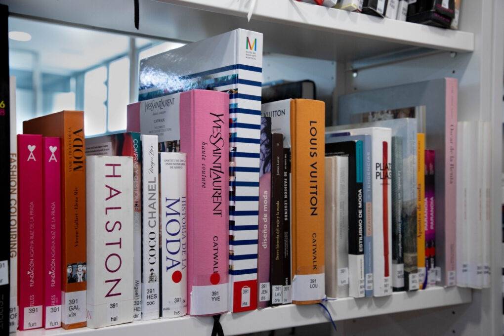 Una estantería con libros de moda y diseñadores famosos.