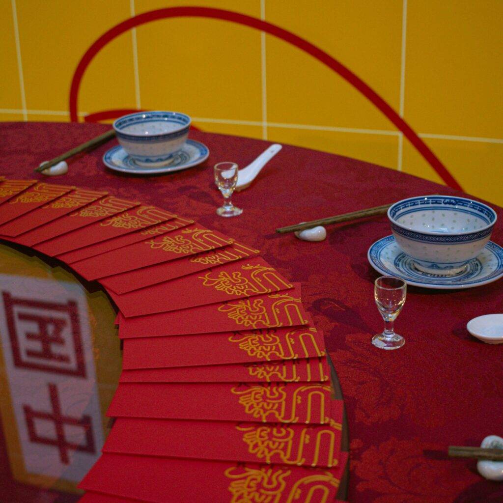 La imagen muestra una mesa decorada con platos, tazas y sobres rojos en un ambiente festivo.