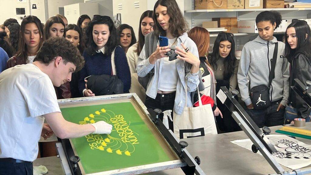 Un grupo de estudiantes observa a una persona haciendo serigrafía en una clase.