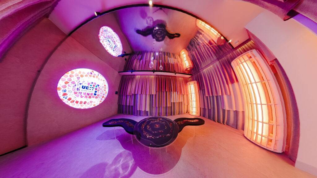 Una habitación circular con paredes decoradas y ventanas coloridas que emiten luz suave.