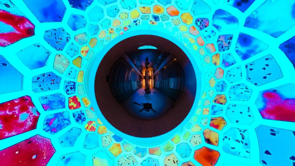 La imagen muestra un pasillo iluminado con luces azules y un diseño de hexágonos coloridos en el techo.