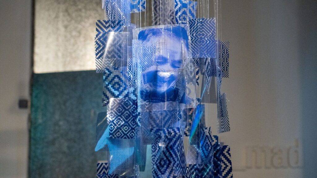 Una instalación artística suspendida compuesta por imágenes en tonos azules y patrones geométricos.