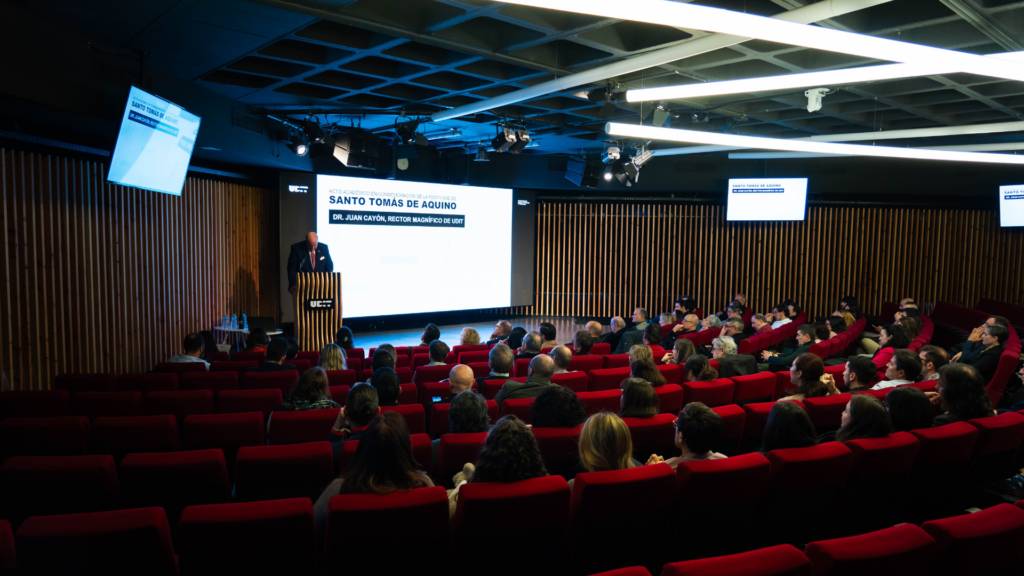 Un orador presenta un discurso ante una audiencia en un auditorio con asientos rojos.