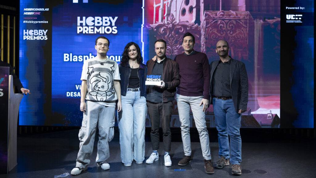 Un grupo de cinco personas posando en un escenario durante un evento de premios, sosteniendo un trofeo.