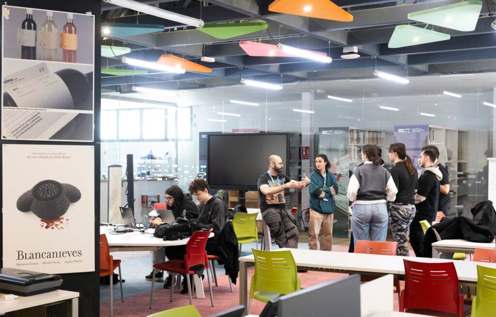 Un grupo de personas discutiendo en un espacio de trabajo moderno con mesas y tecnología visible.