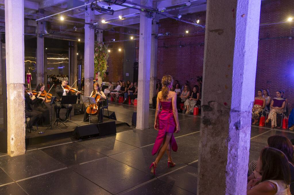 Una modelo desfila en una pasarela mientras un cuarteto de cuerdas toca música en un evento de moda.