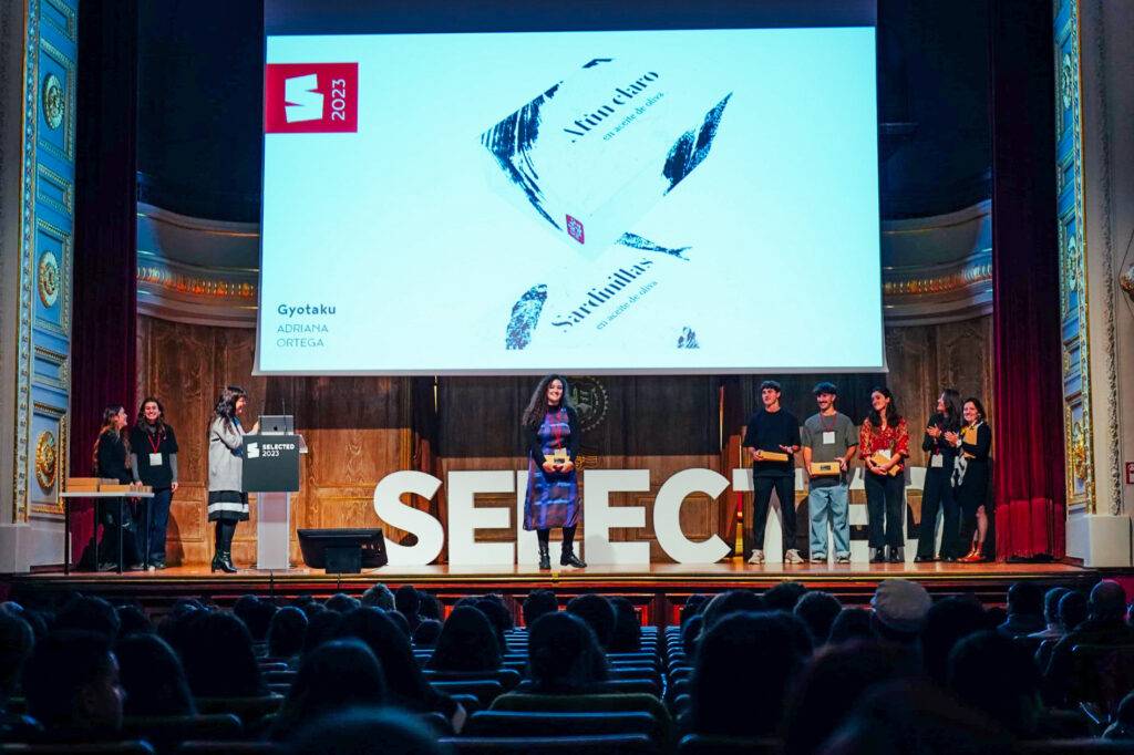 Evento de presentación en un escenario con diversas personas y un panel informativo en el fondo.