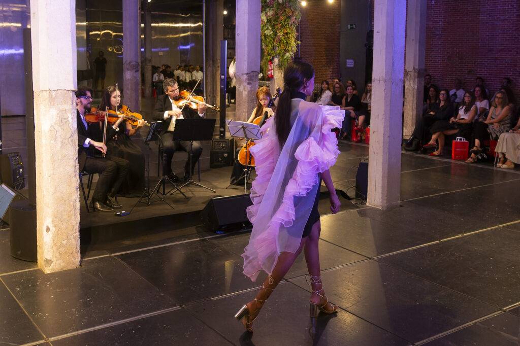 Una modelo camina por una pasarela mientras un grupo de músicos toca en vivo.