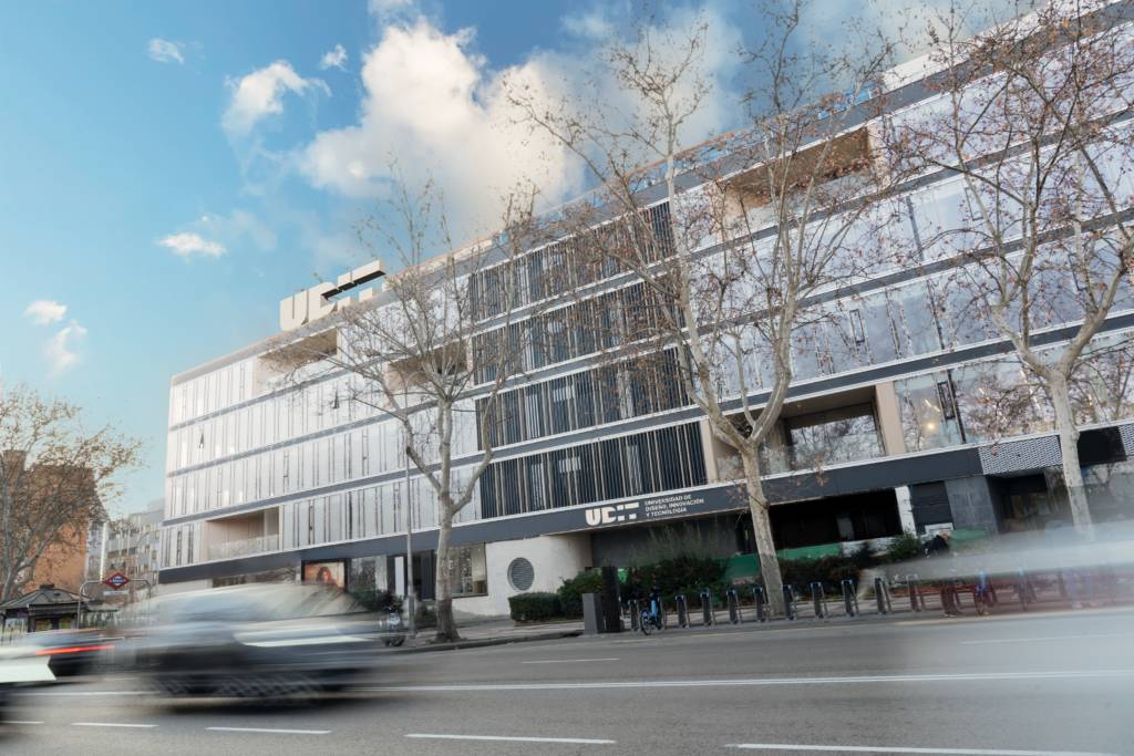 Edificio moderno con fachada de vidrio y árboles en la calle.