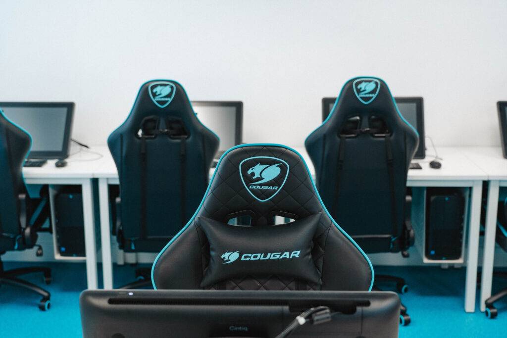 Una sala de trabajo con sillas de gaming Cougar y computadoras en la mesa.