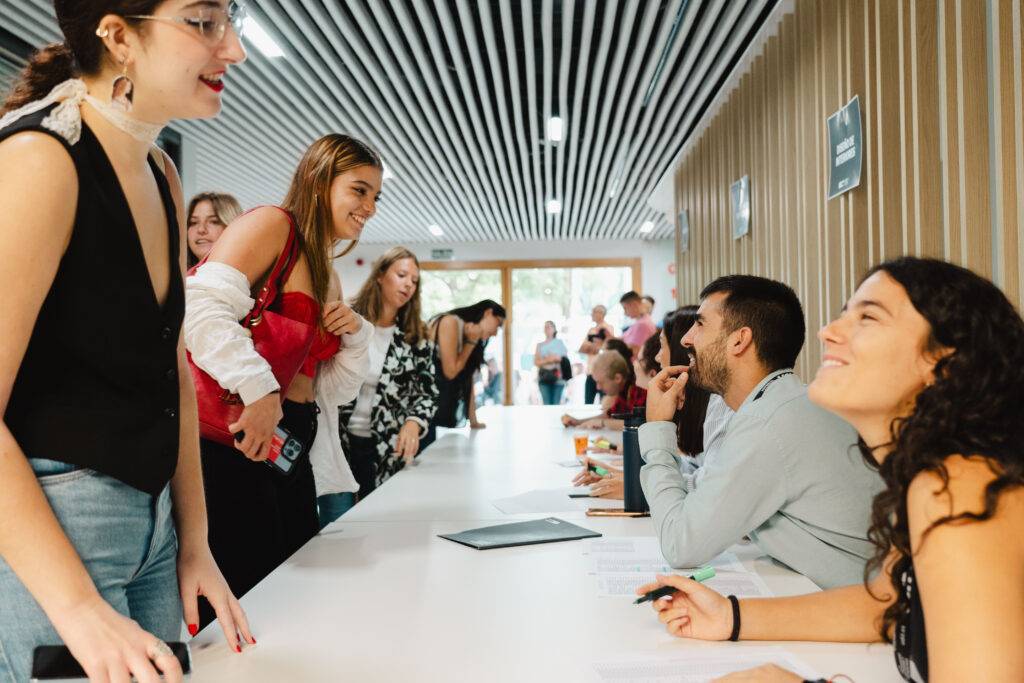 Un grupo de personas en un evento social, algunas sonriendo y conversando mientras hacen fila para registrarse.