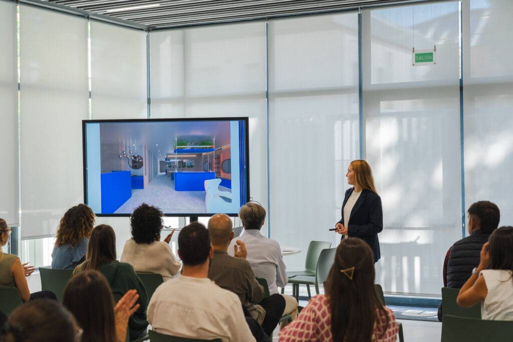 Una mujer presenta un proyecto en una reunión frente a un público en un ambiente moderno.