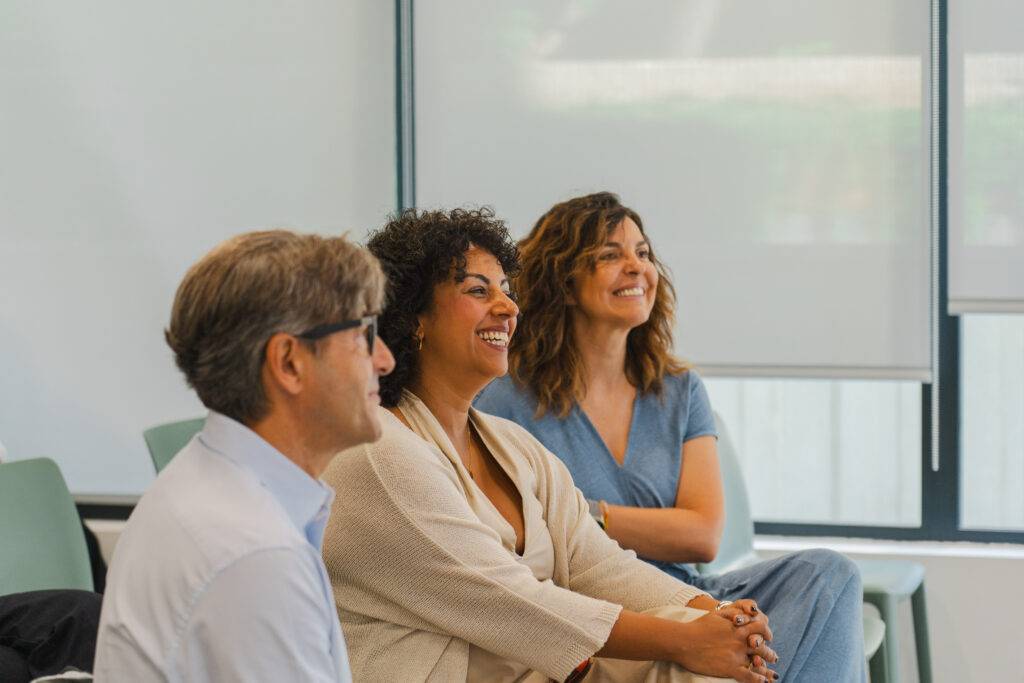 Un grupo de personas sonríe mientras escucha una presentación.