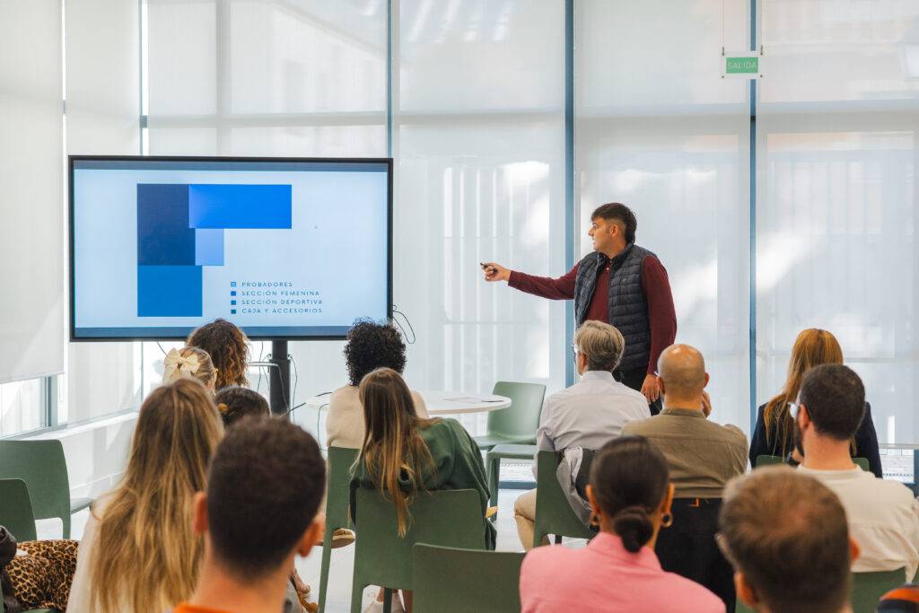 Un presentador expone información en una pantalla mientras un grupo de personas lo observa atentamente.
