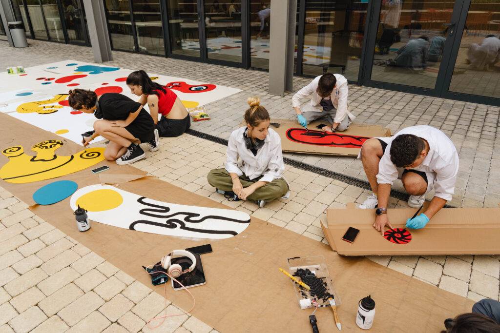 Un grupo de personas está pintando en una superficie al aire libre con colores vivos y diseños variados.