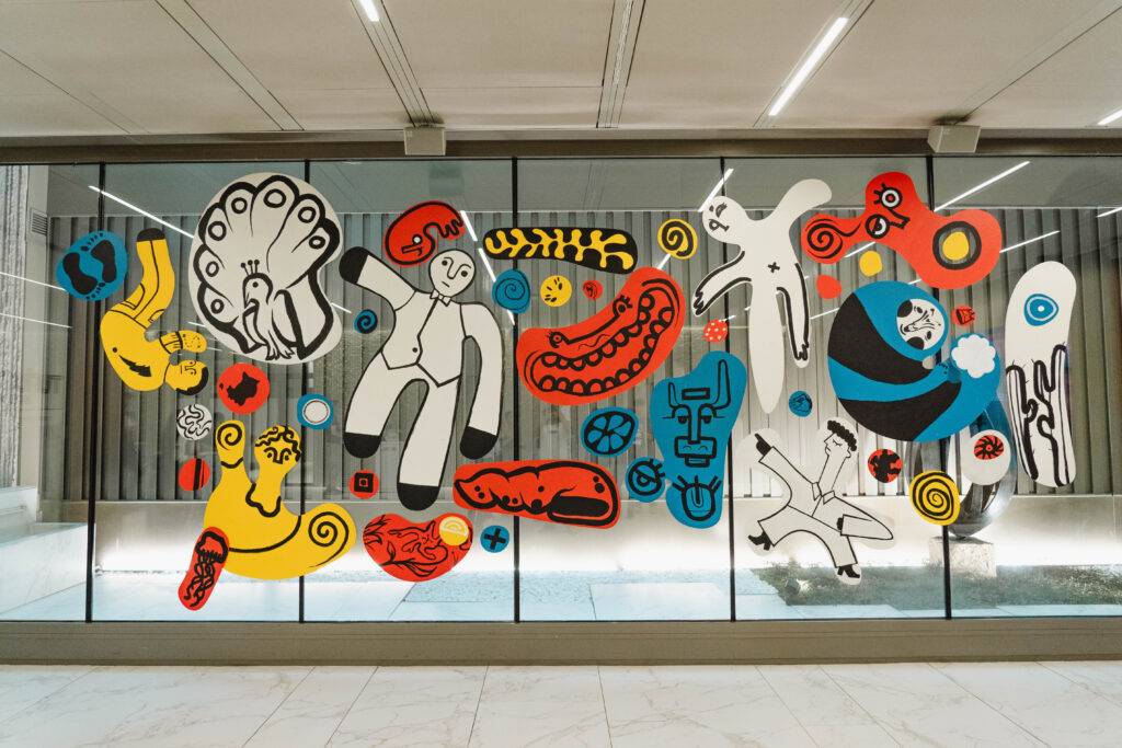 Un mural colorido con formas abstractas y figuras estilizadas en una pared de vidrio.