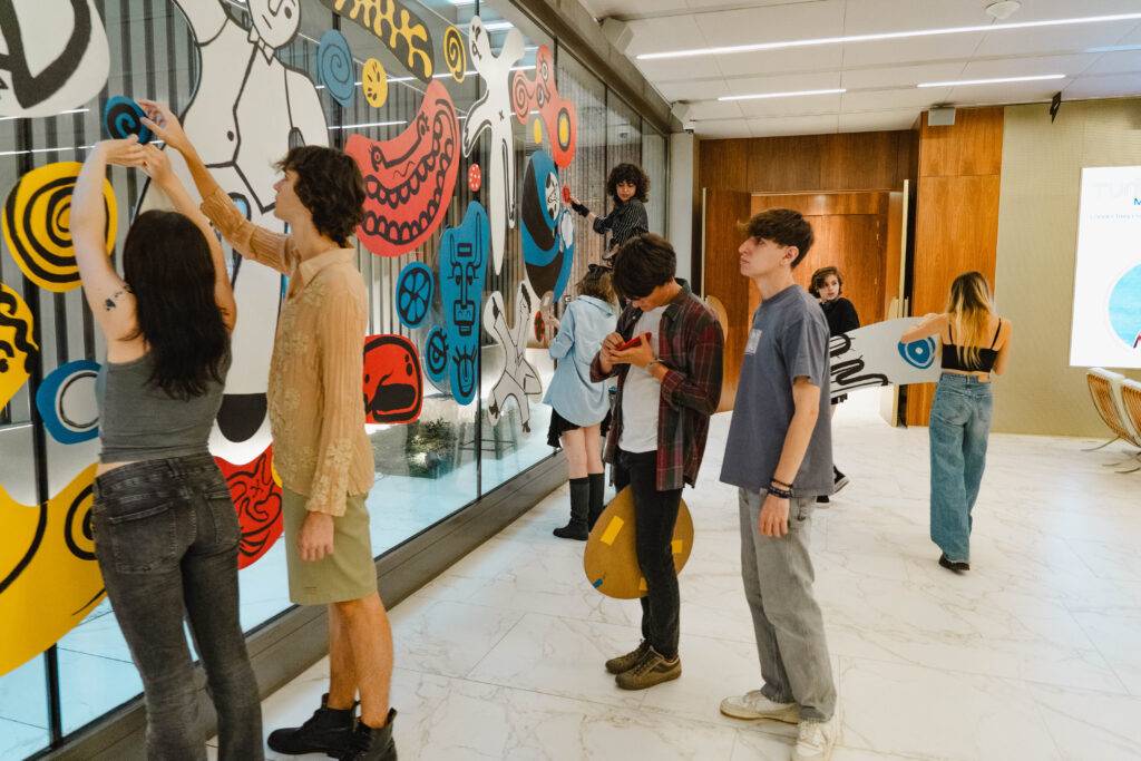 Un grupo de personas está colaborando para pintar un mural en una oficina moderna.
