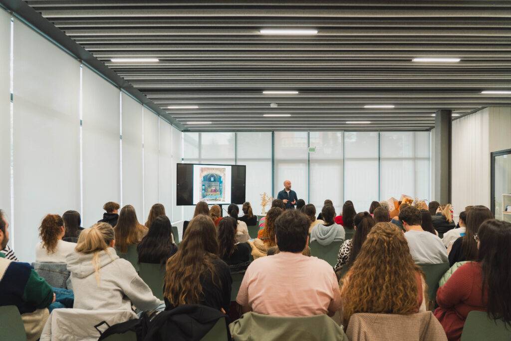 Un grupo de estudiantes escucha a un ponente en un aula moderna con grandes ventanales.