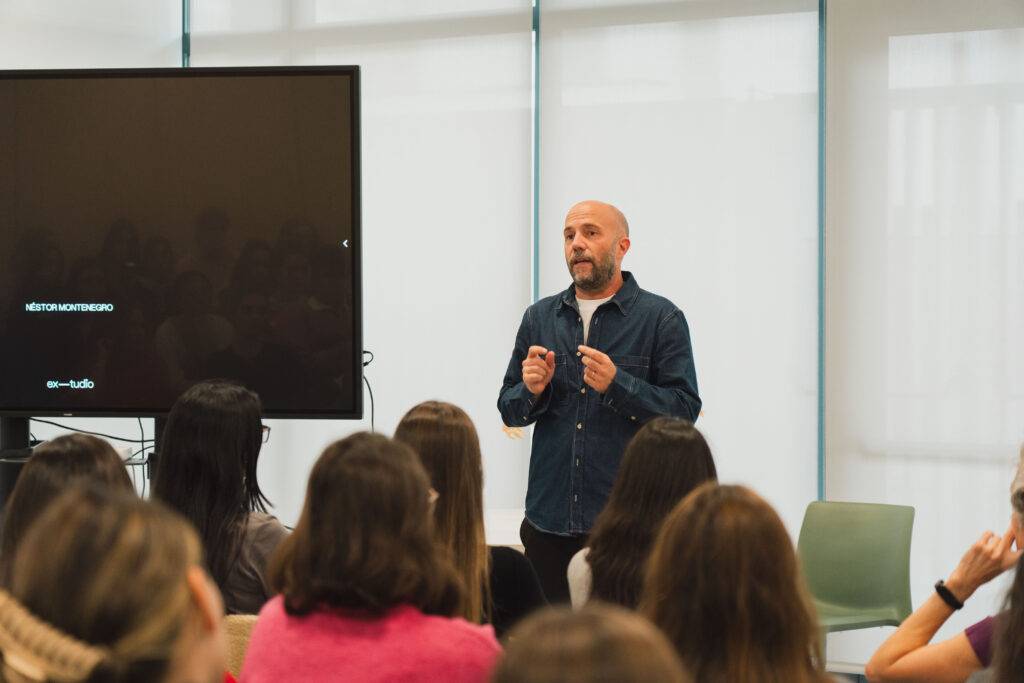 Un hombre está dando una charla frente a una audiencia sentada en un salón con pantallas en el fondo.