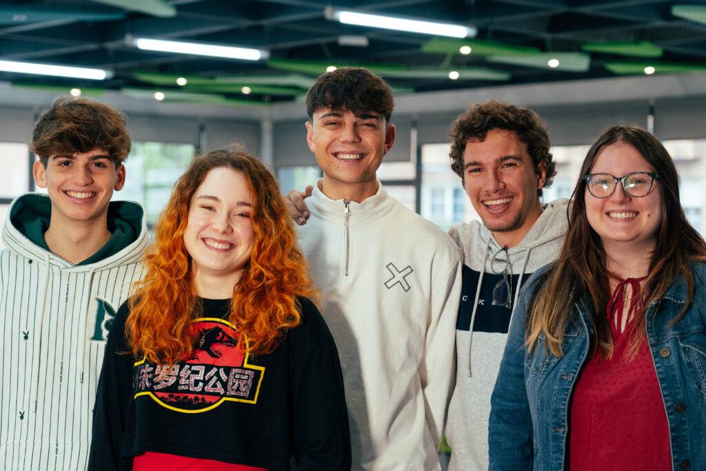 Un grupo de cinco jóvenes sonrientes posan juntos en un ambiente iluminado.
