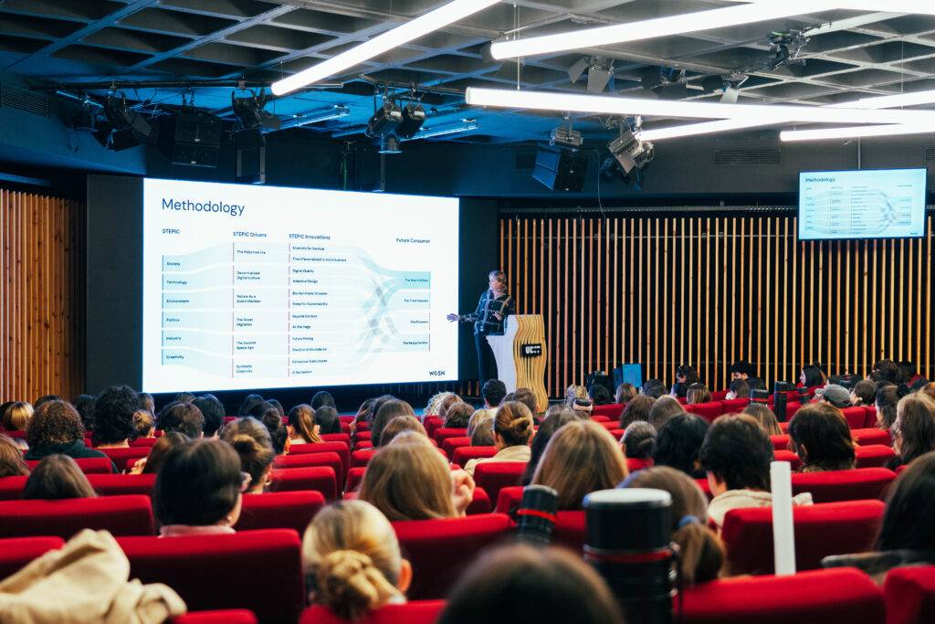 Un presentador habla frente a una audiencia en un evento, mientras se proyecta una diapositiva sobre metodología.