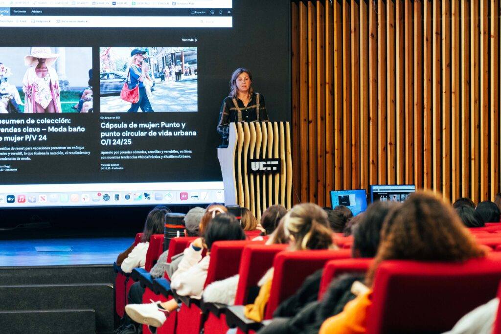Una mujer presenta un evento en un auditorio frente a un público atento.