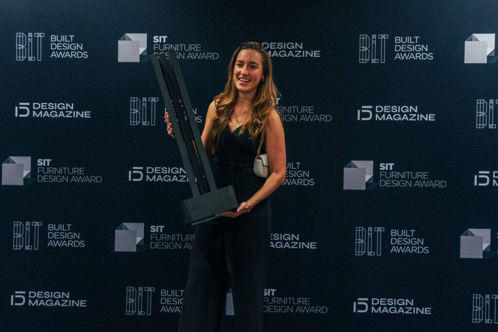 Una mujer sonriente sostiene un premio en un evento de diseño.