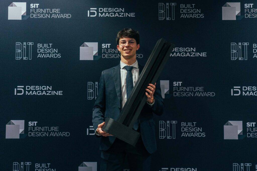 Un joven elegante sostiene un galardón en un evento de premiación de diseño.