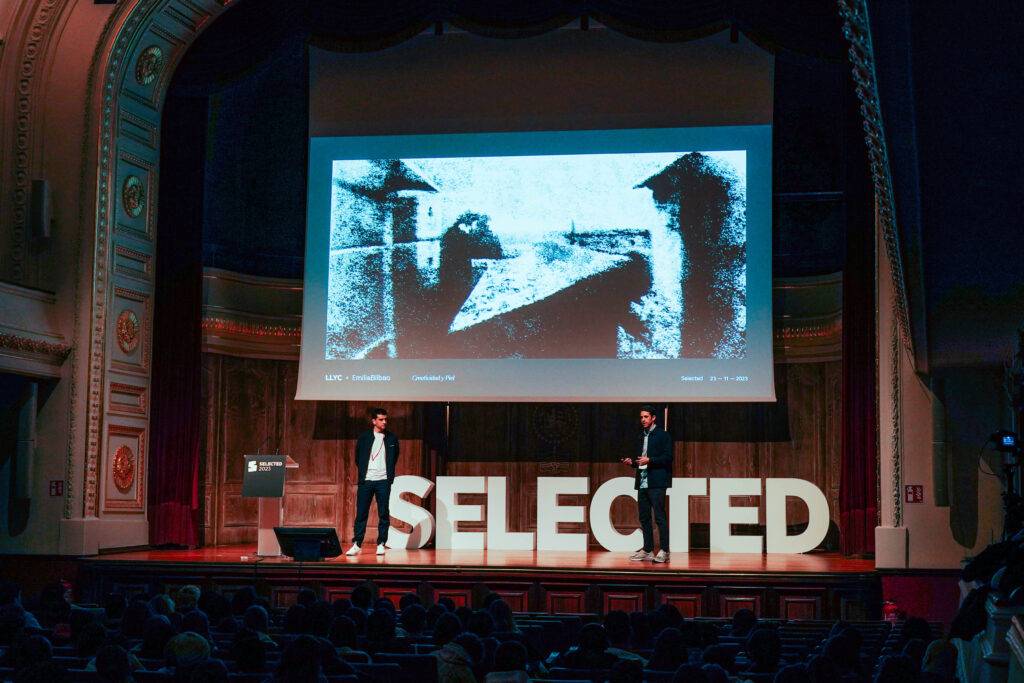 Una presentación en un auditorio con una imagen en la pantalla y el título 'SELECTED'.