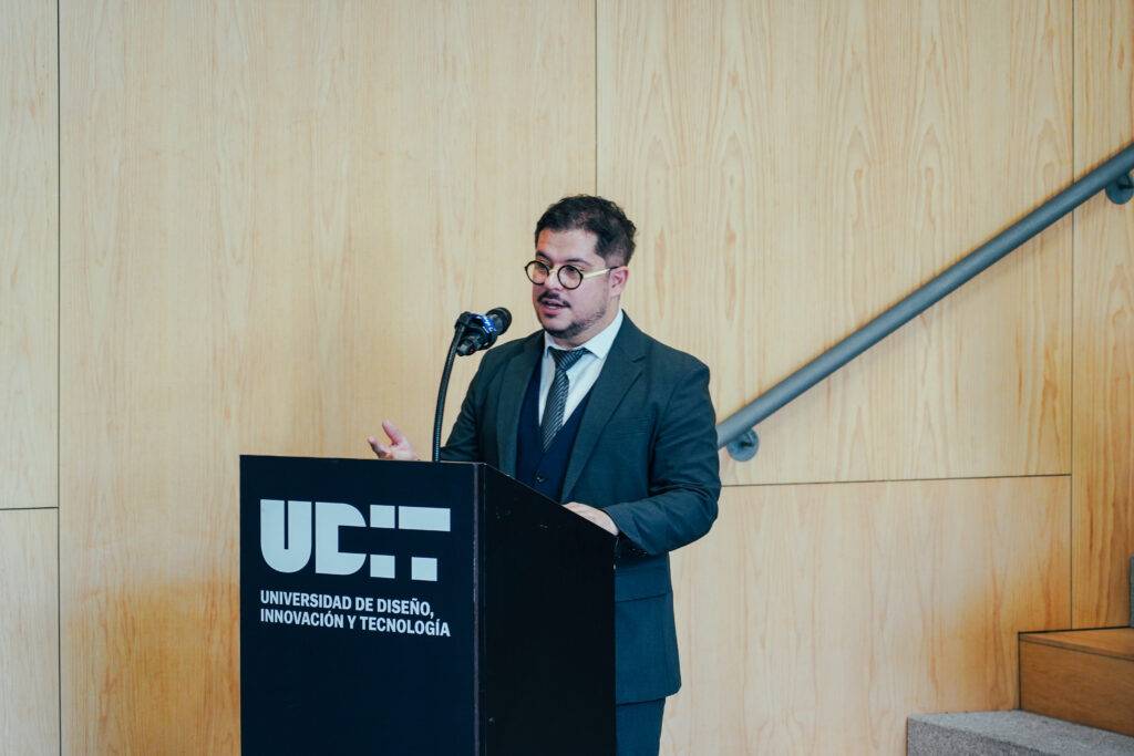 Un hombre con gafas y traje está hablando frente a un micrófono en un evento en la Universidad de Diseño, Innovación y Tecnología.