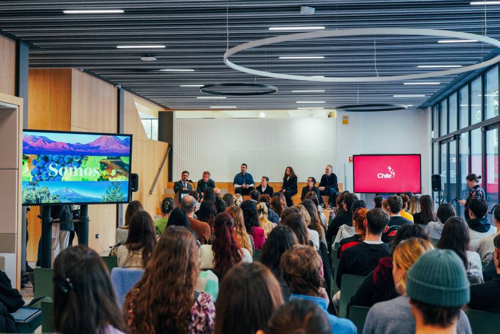 Una conferencia con un panel de oradores y un público atento en un entorno moderno.