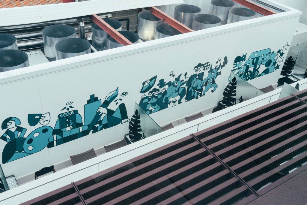 La imagen muestra un mural artístico colorido en una pared exterior con diversas figuras y formas abstractas.