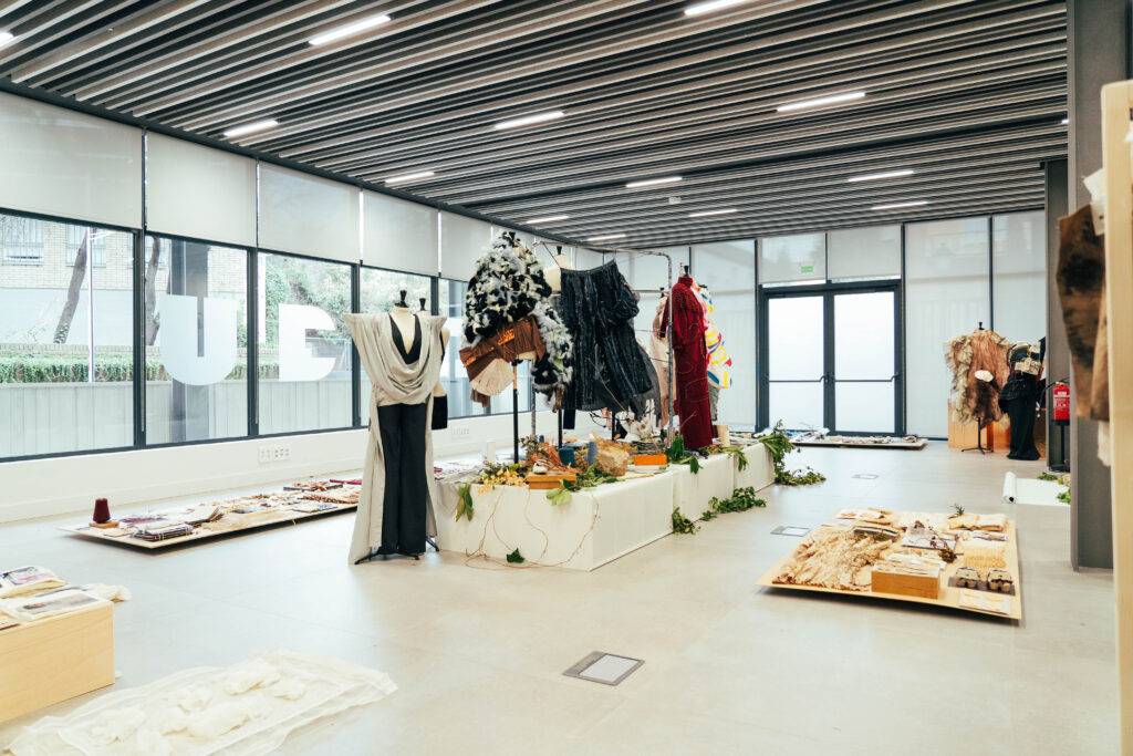 La imagen muestra un espacio de exhibición con diversas prendas de vestir y elementos decorativos dispuestos de manera artística.