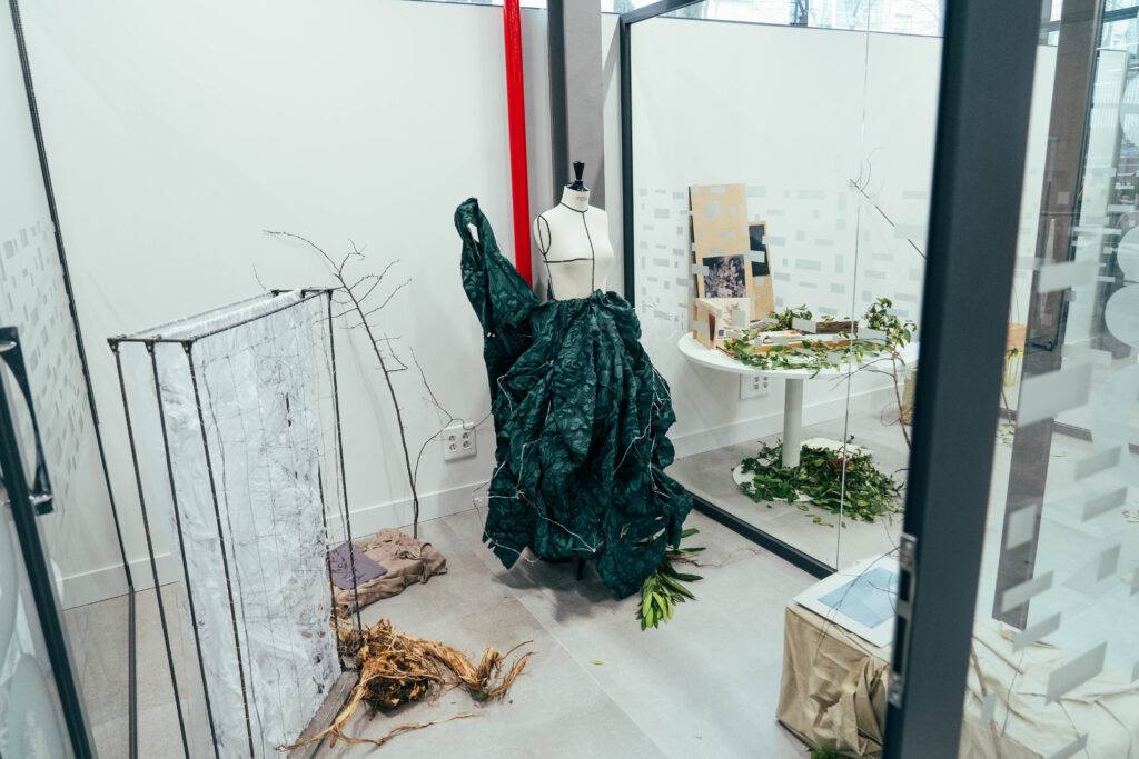 Una exhibición artística que presenta un vestido verde sobre un maniquí en un entorno natural.