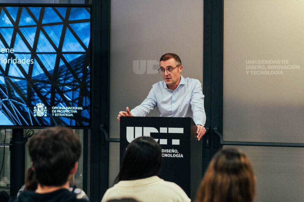 Un orador presenta en una conferencia frente a un público en una universidad de diseño y tecnología.
