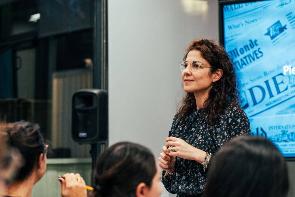 Una mujer está dando una charla frente a un grupo de personas en un ambiente moderno.