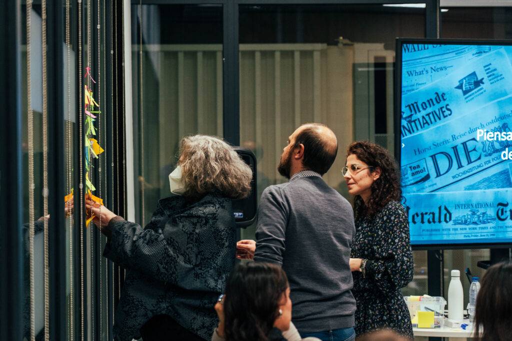 Un grupo de personas interactúa en un ambiente de trabajo mientras organizan notas adhesivas en una pared.