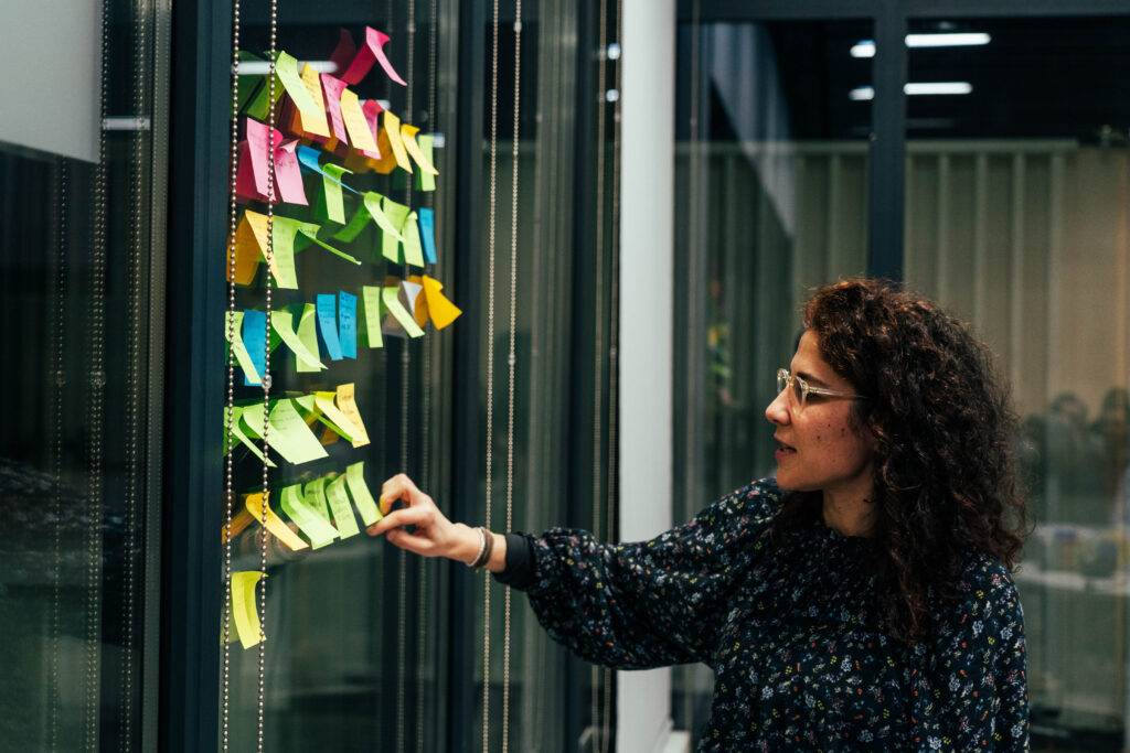Una mujer organiza notas adhesivas de diferentes colores en una pared de cristales.