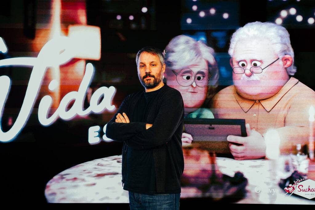 Una persona posa frente a una pantalla con una animación de personajes mayores en un ambiente acogedor.