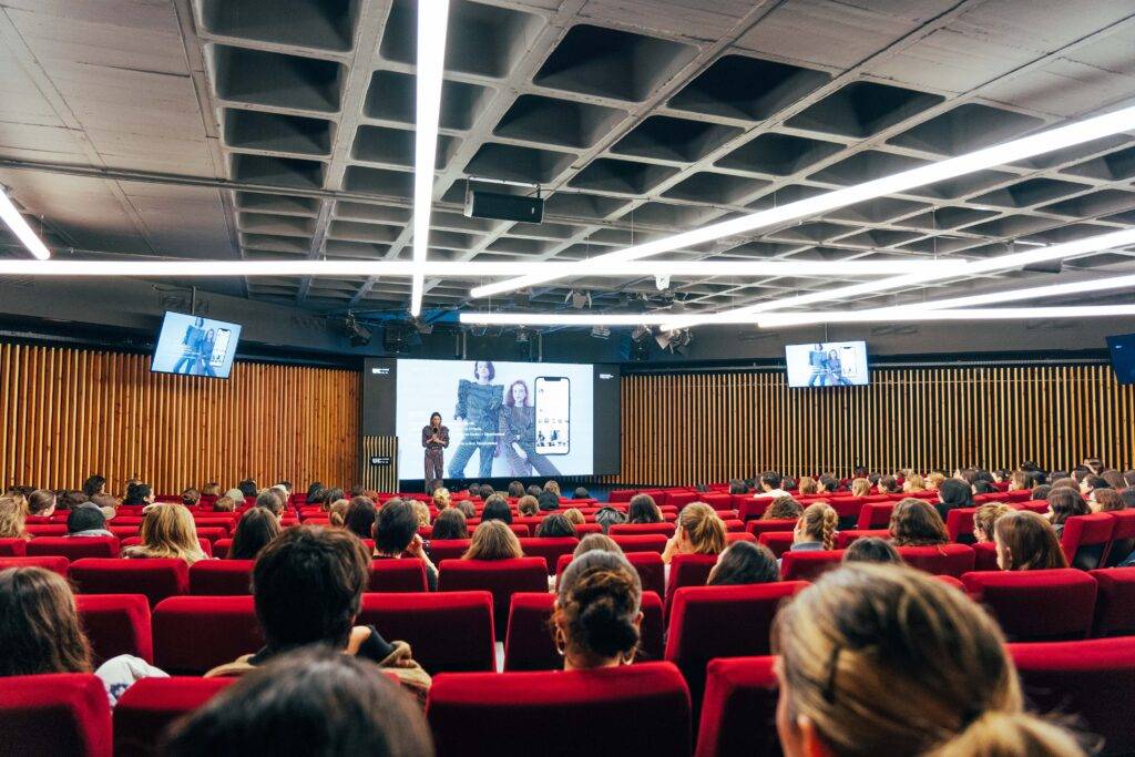 Una conferencia con un orador frente a una audiencia en un auditorio moderno.