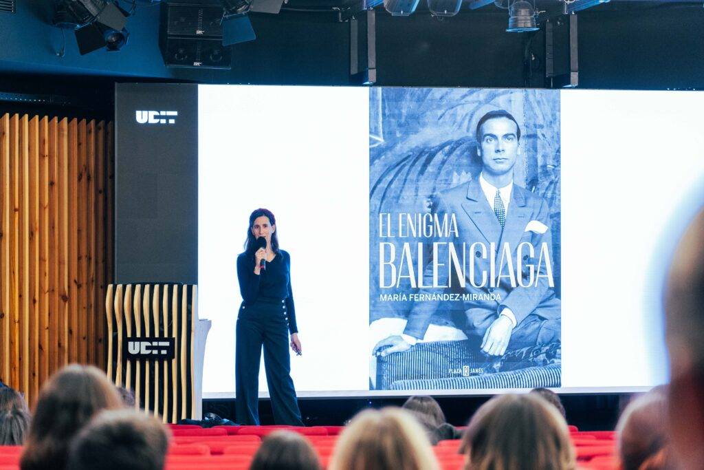 Una mujer presenta un libro sobre Balenciaga en un auditorio.