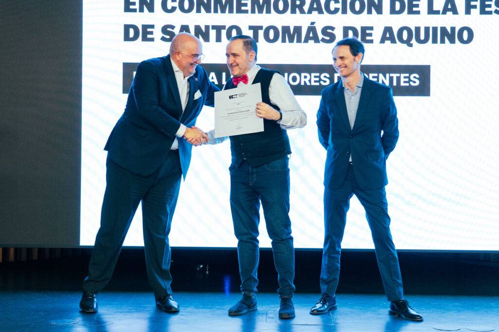 Un grupo de tres hombres en una ceremonia de premiación se están dando la mano mientras uno de ellos sostiene un certificado.