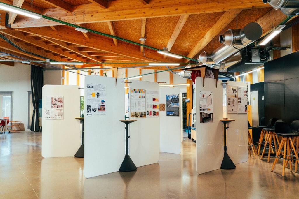 La imagen muestra un espacio interior con paneles de exhibición y mesas altas alrededor en un ambiente moderno y luminoso.